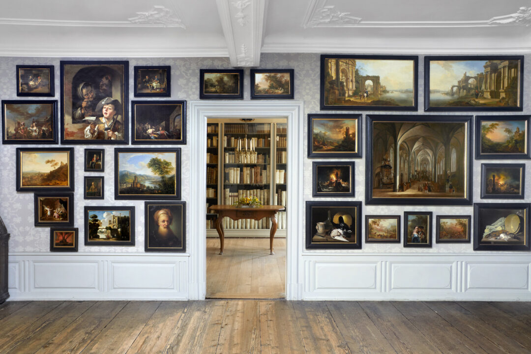 Frontaler Einblick in das Gemäldekabinett des Goethe Hauses. rechts und links hängen verschiedene Gemälde, gerade aus ist ein Zimmer mit verschiedenen Büchern zu sehen. 