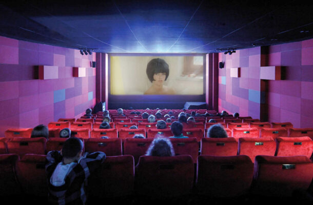 Kinder sitzen in einem Kinosaal mit roten Stühlen