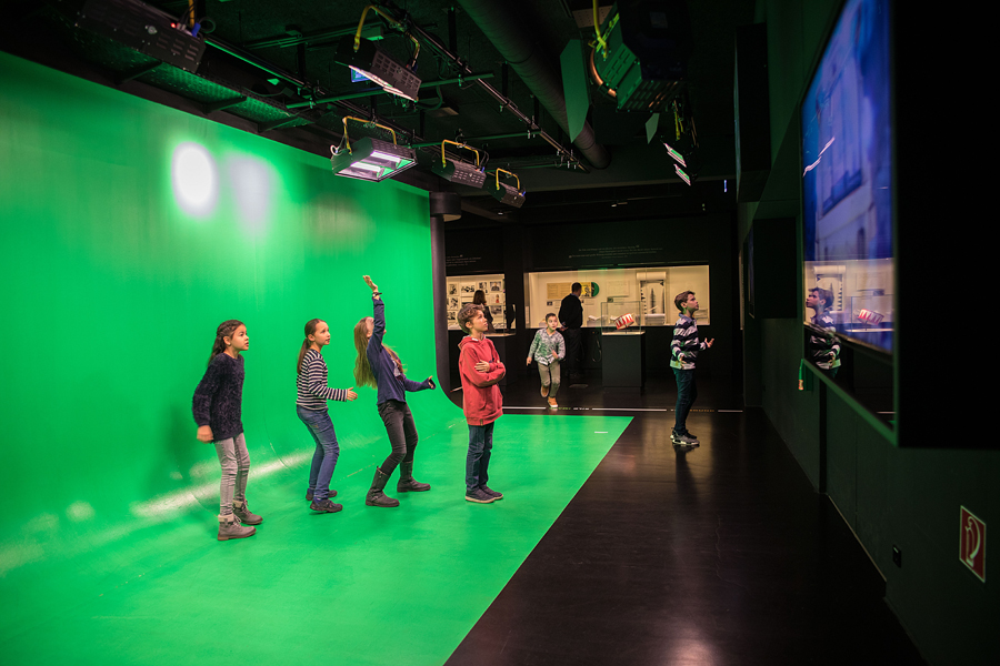 4 Kinder stehen in einem grünen Studio mit Scheinwerfer und Kamera